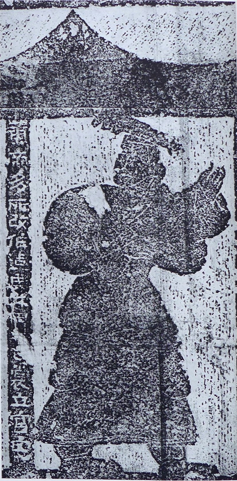 Ink rubbing of a Han-dynasty carved stone relief from the Wu Family Shrines showing the Yellow Emperor as a robed standing sovereign beneath a gabled canopy, one hand raised, a vertical cartouche of incised characters down the left edge naming him and his inventions; the figure and inscription read as light forms against the mottled dark ground of the rubbing.