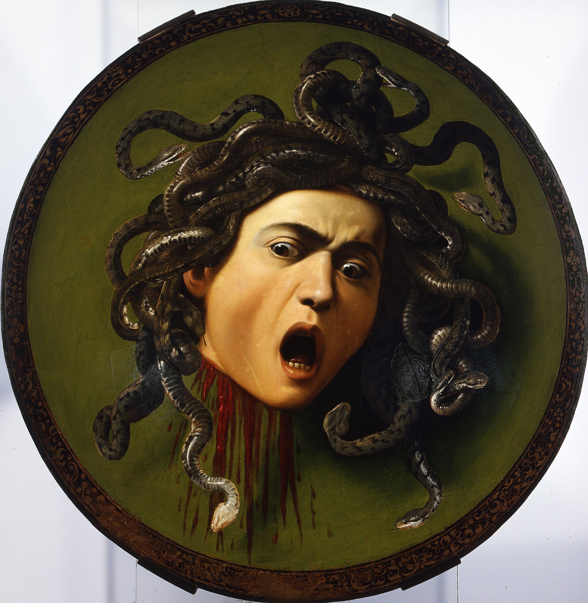 A severed, snake-haired head with wide staring eyes and mouth open in a scream, blood streaming from the neck, dark serpents writhing outward from the scalp against a green convex ground ringed by a gilt border — Caravaggio's Medusa, painted on a ceremonial parade shield, showing the Gorgon's face in the instant after decapitation.