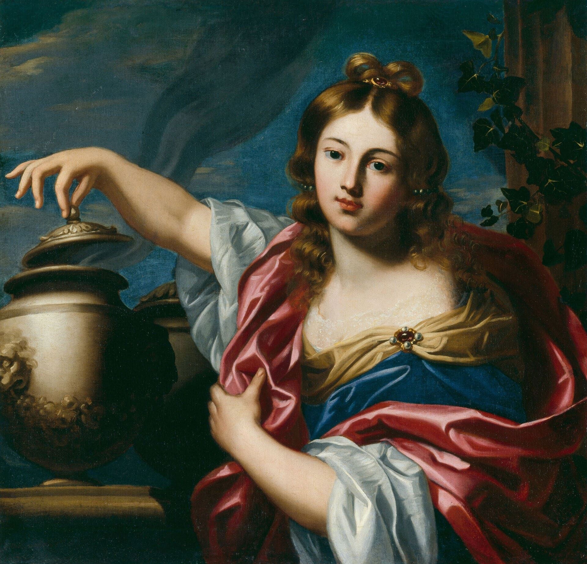 A young woman with loose auburn hair, in a blue gown under a rose-red mantle with a jewelled clasp, rests her right hand on the ornamented lid of a great lidded ceramic jar at the left — a satyr-mask moulded on its swelling belly — as if about to lift it; ivy climbs a broken pillar behind her against a stormy blue sky.